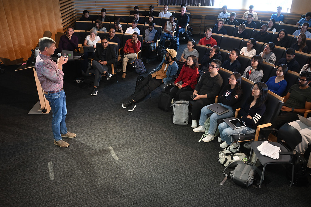A speaker addressing a packed lecture hall of students.